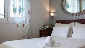 A neatly made bed with a white duvet, a bedside table with a vase of flowers, and a round mirror on the wall.