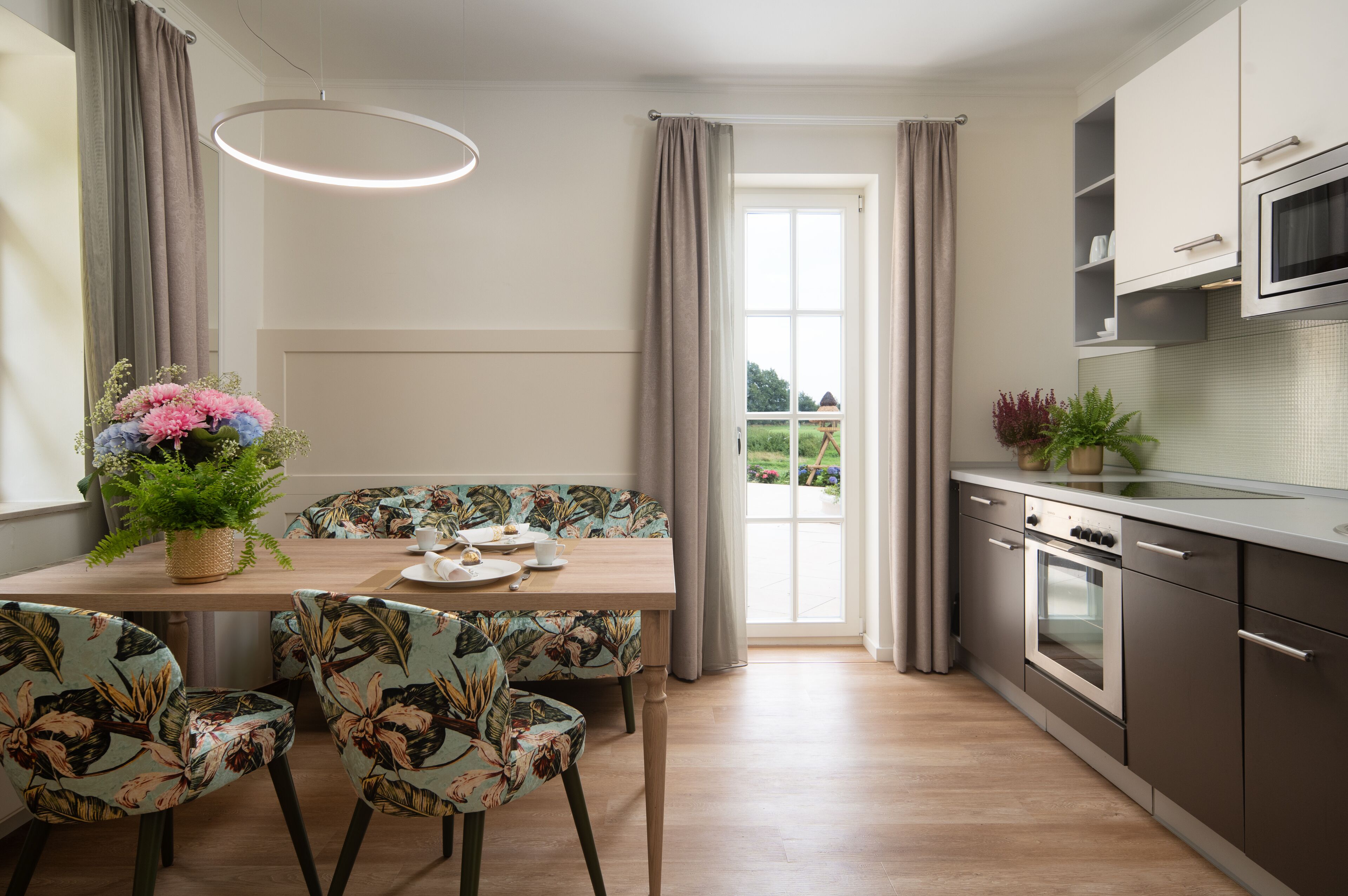 Una cocina moderna con comedor, que incluye una mesa de madera, sillas con estampado floral y un horno empotrado.