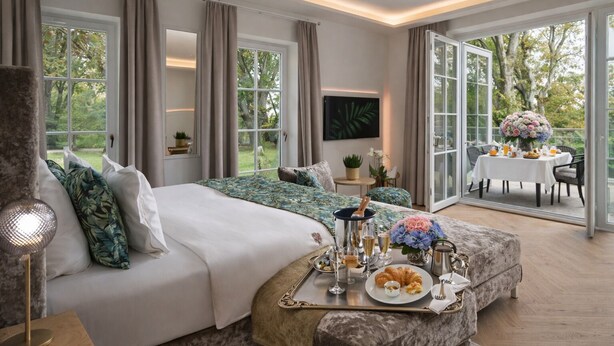 A spacious bedroom with a large bed, a dining area with a table set for two, and a view of the outdoors. - Schlossresidenz Boutique Apartements & Hotel Suiten (Garbsen)