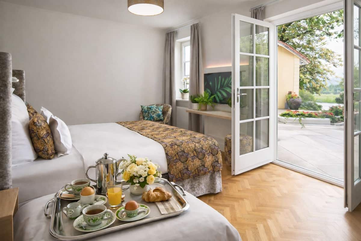 Une chambre d’hôtel avec un lit, un plateau de petit-déjeuner et une vue sur le jardin par une porte ouverte.