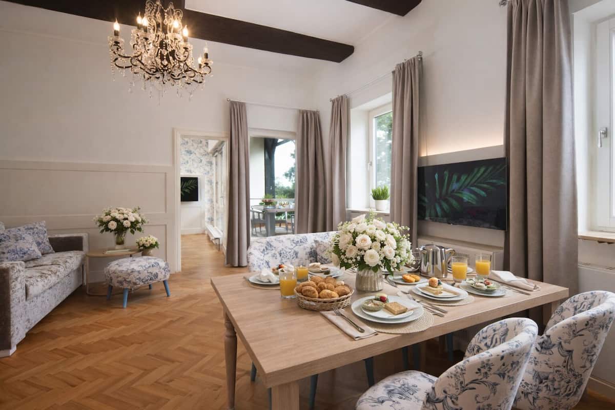 Un coin repas avec une table en bois dressée pour le petit-déjeuner, agrémentée de compositions florales et surmontée d’un lustre.
