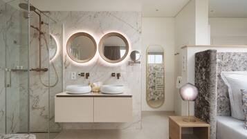 A modern bathroom with a glass-enclosed shower, a marble vanity with two sinks, and a round mirror with integrated lighting.