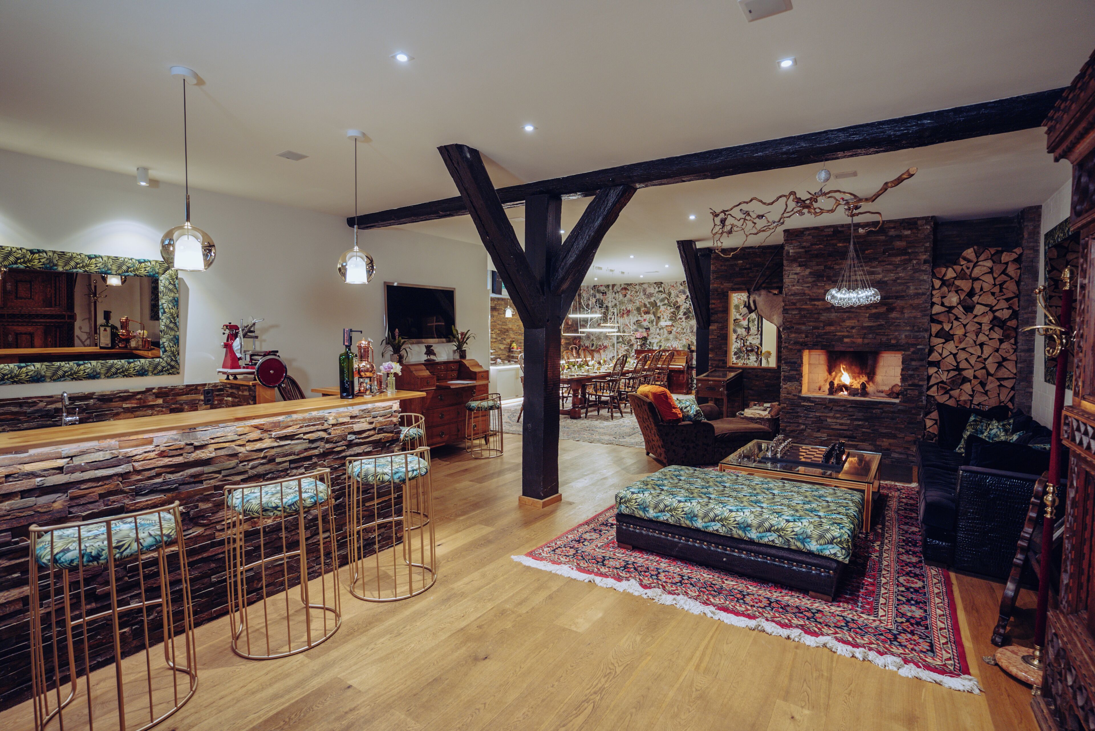 A spacious living area with a stone fireplace, wooden beams, and a bar with stools.