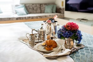 A breakfast setup with a croissant, a bottle of champagne, and a vase of flowers on a tray. - Schlossresidenz Boutique Apartements & Hotel Suiten (Garbsen)
