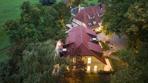 A large house with a red roof, surrounded by trees and a green field. - Schlossresidenz Boutique Apartements & Hotel Suiten (Garbsen)