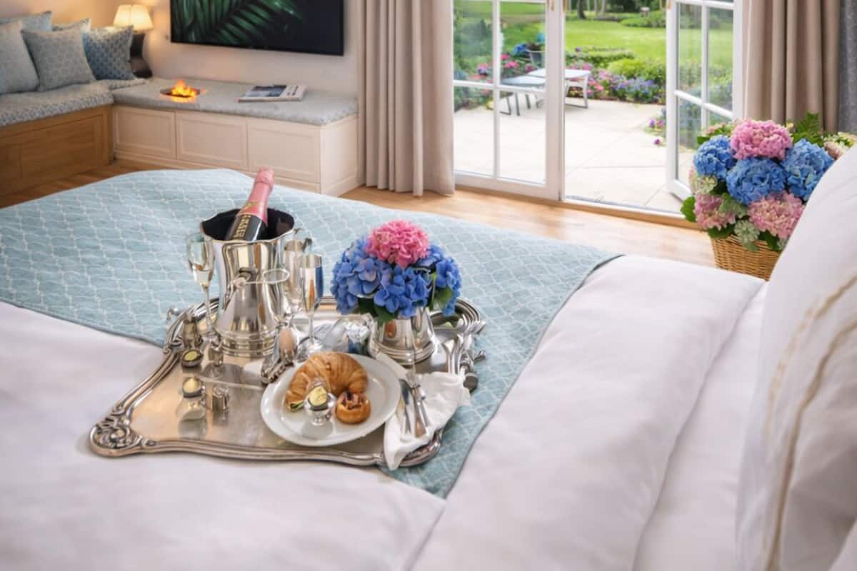 Une chambre avec un grand lit, une télévision, une table de chevet avec une lampe et une vue sur un jardin, visible à travers une porte vitrée.