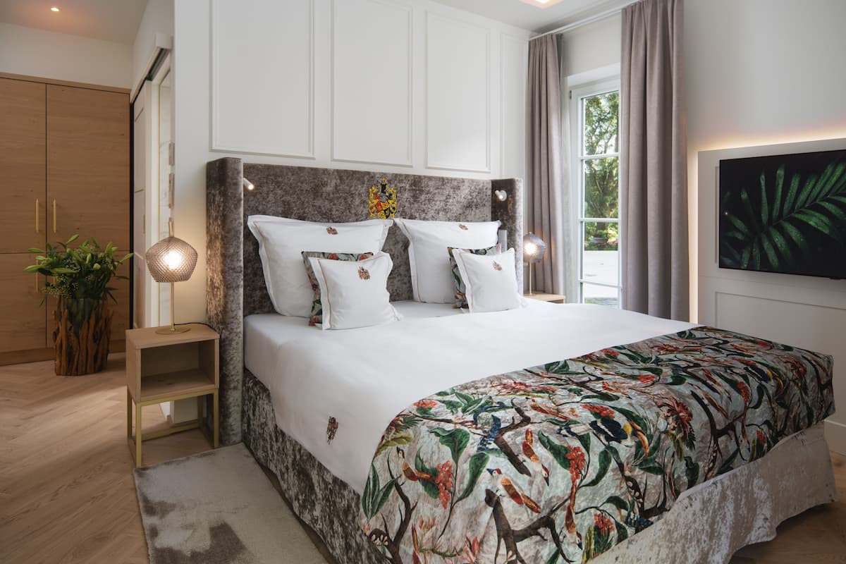 Une chambre à coucher avec un grand lit, une armoire en bois, une table de chevet avec une lampe et une grande fenêtre avec des rideaux.