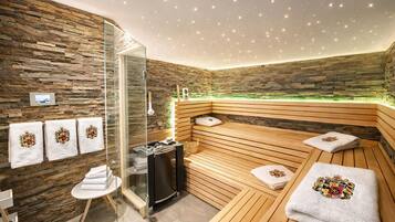 Une salle de spa moderne avec un mur en pierre, des sièges en bois, une douche en verre et des serviettes ornées d’un motif héraldique.