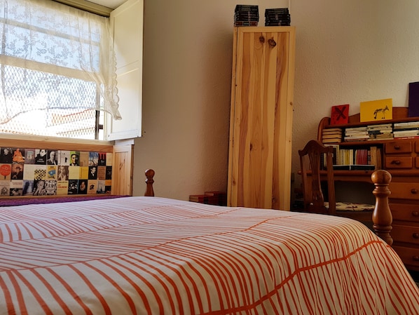 A bedroom with a bed, a wooden wardrobe, a bookshelf, and a window with lace curtains. - Ratones de Biblioteca - Hostel (San Cristóbal de La Laguna)