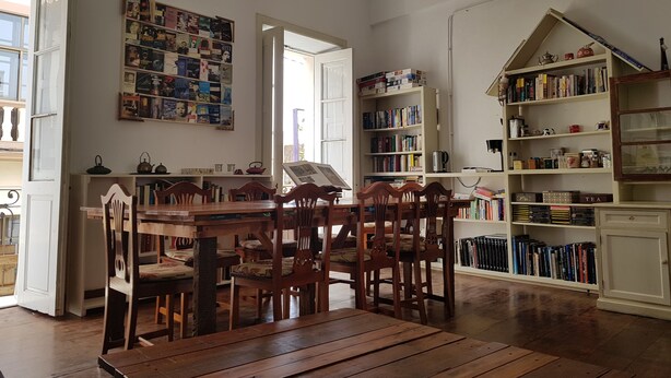 Une pièce comprenant une table et des chaises en bois, une bibliothèque remplie de livres et un mur décoré de divers objets.