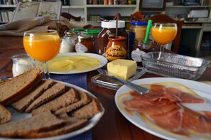 Una mesa de desayuno con pan, mantequilla, jamón y jugo de naranja.