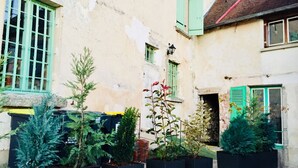 Une cour intérieure agrémentée de plantes en pot et un bâtiment aux volets verts et à la façade patinée.
