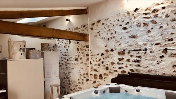 Un espace spa comprenant un jacuzzi, un mur en pierre, des poutres en bois et un petit coin bar.