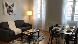 A modern living room with a grey sofa, a coffee table with magazines, a dining table set for four with chairs, a lamp, and a painting on the wall. - CENTER - SPACIOUS - COZY - WIFI (Albi)