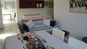 A living room with a sofa, a dining table with a decorative item, and a framed picture on the wall. - Bright house with garden and terraces. (Concarneau)