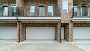 A two-story building with a brick facade, two garage doors, and a balcony with metal railings. - 10 mins from IAH / King Bed - Spacious 2 Bedroom home - Unit B (Humble)