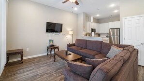 A modern living room with a brown sectional sofa, a wooden coffee table, and a ceiling fan. - 10 mins from IAH / King Bed - Spacious 2 Bedroom home - Unit B (Humble)