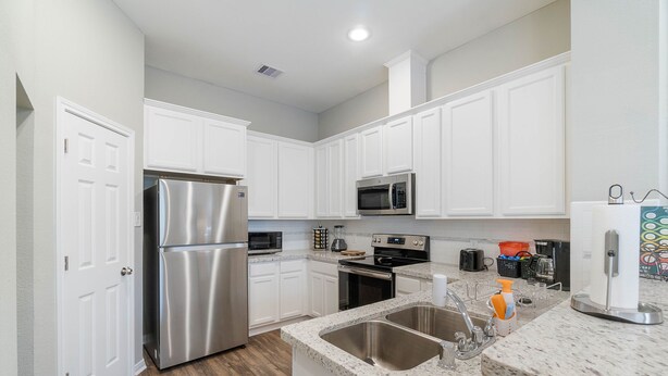 A modern kitchen with white cabinets, stainless steel appliances, a granite countertop, and a double sink. - 10 mins from IAH / King Bed - Spacious 2 Bedroom home - Unit B (Humble)