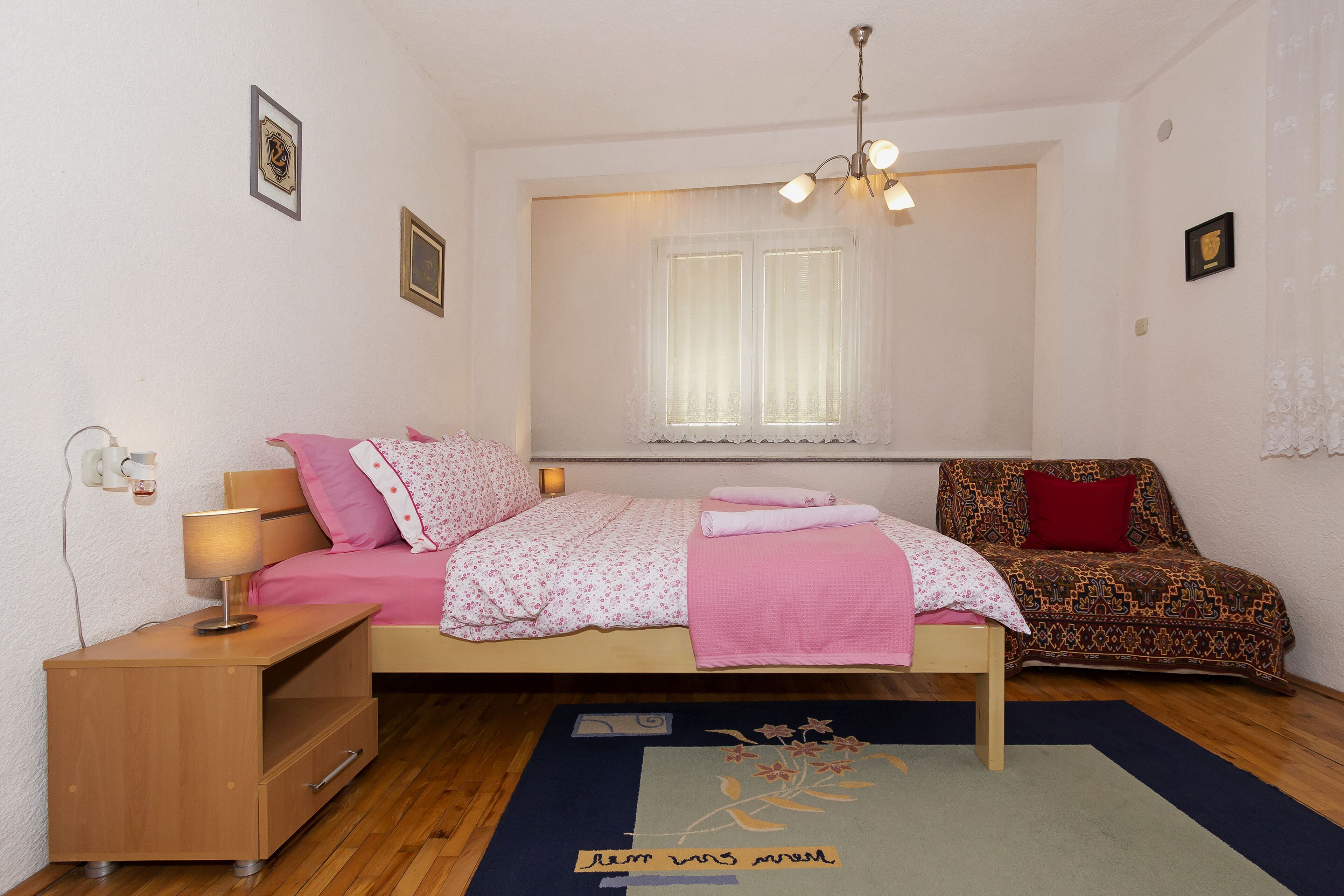Un dormitorio con cama, mesita de noche, lámpara y ventana con cortinas.