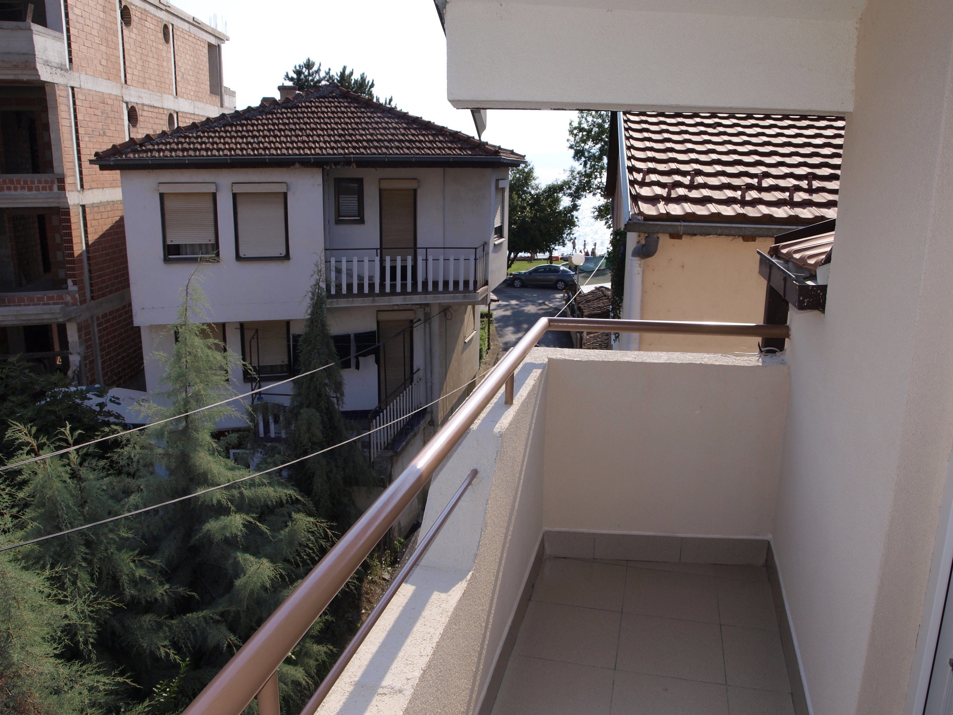 A balcony with a view of a residential building, a parked car, and a tree.