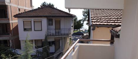 A balcony with a view of a residential building, a parked car, and a tree.