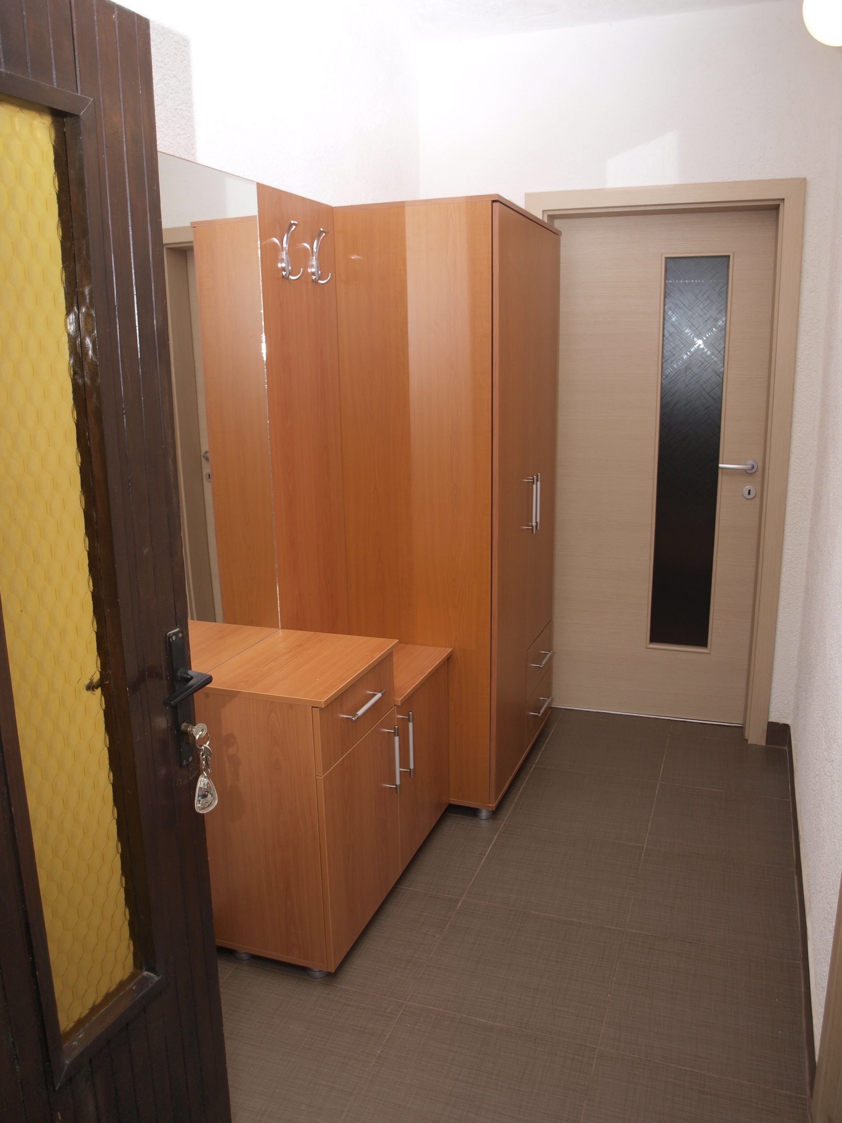 Ein Zimmer mit einem Holzschrank, einem kleinen Holztisch und einer Tür mit Glasfenster.
