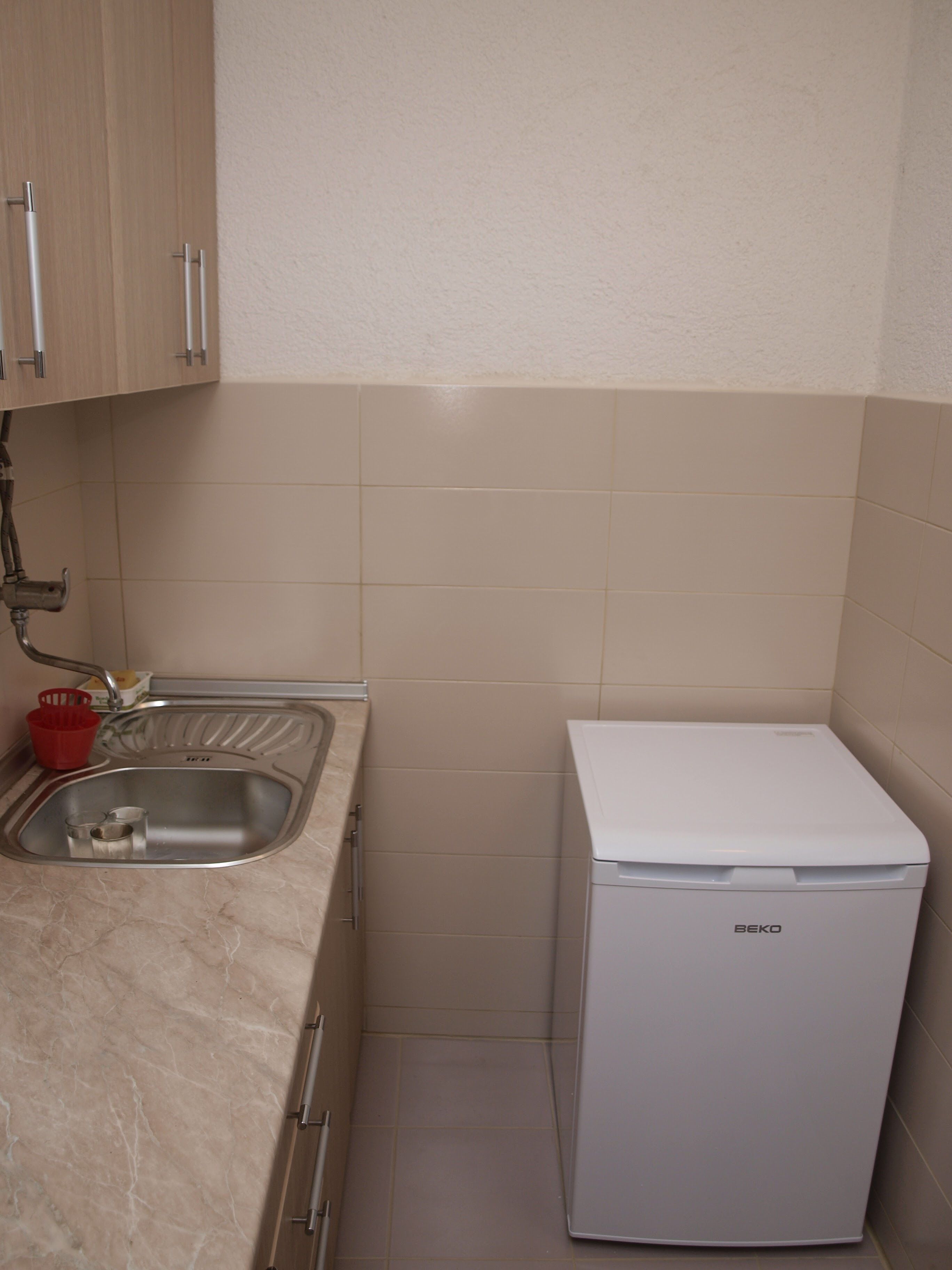 A compact kitchen with a sink, a red basket, and a white appliance.