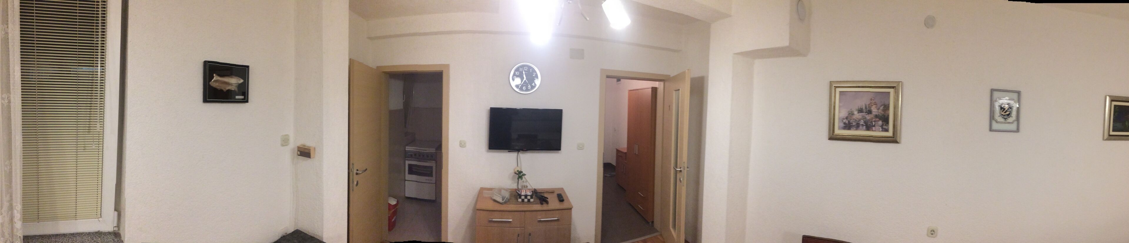 A hallway with a television mounted on the wall, a clock, and framed pictures.