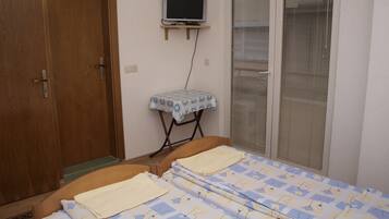Ein Schlafzimmer mit Holztür, einem Fernseher auf einem Schrank, einem Fenster mit Jalousien und einem Bett mit blumigem Überwurf.