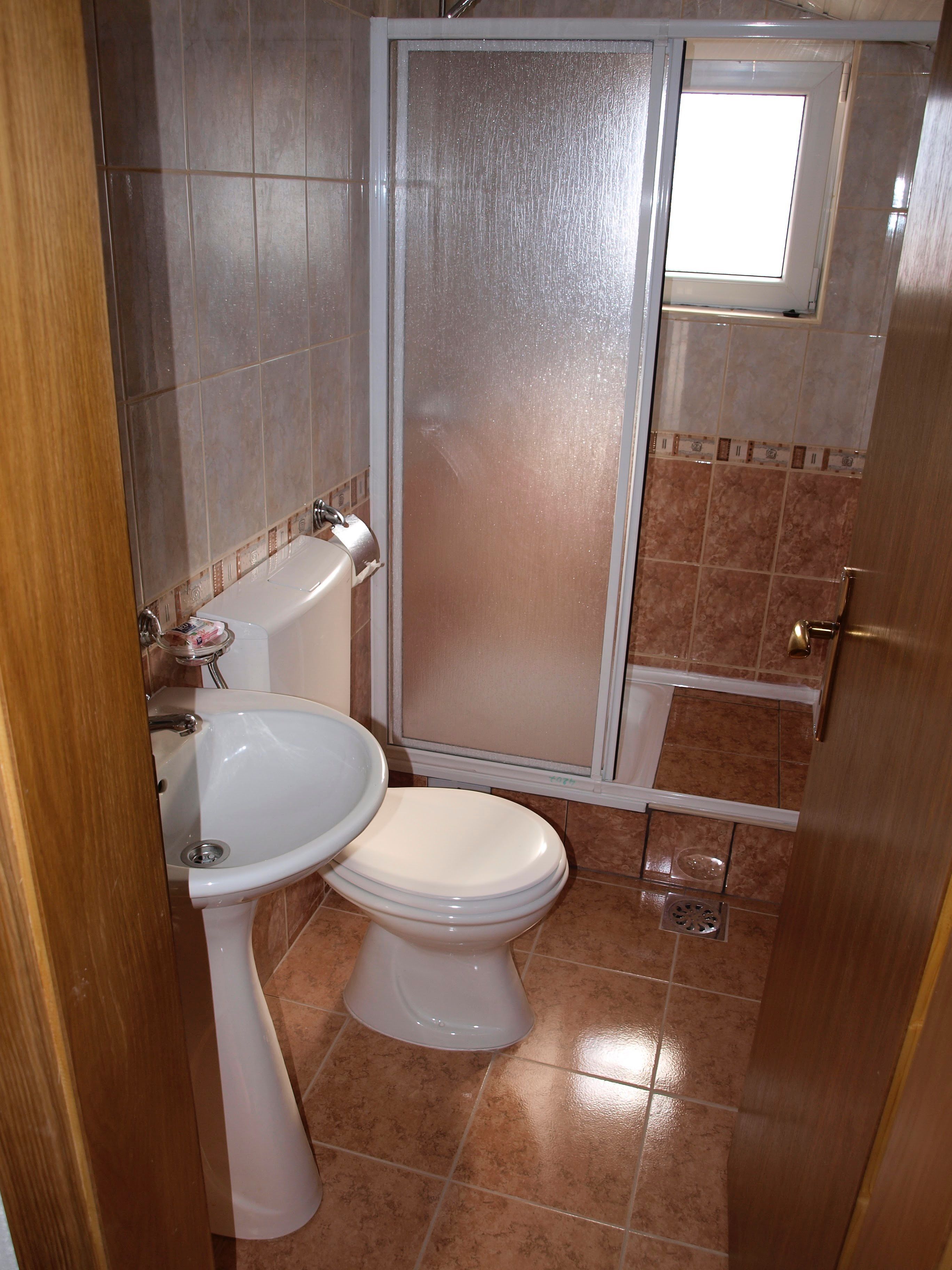 A small bathroom with a toilet, sink, and shower enclosure.