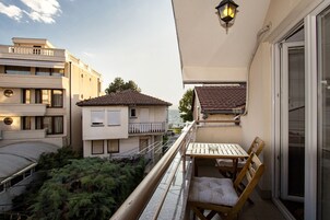 Un balcón con mesa y sillas de madera, con vistas a una zona residencial y un cuerpo de agua.