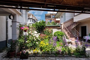 Un patio con plantas y flores en macetas, una escalera y vistas de edificios vecinos.