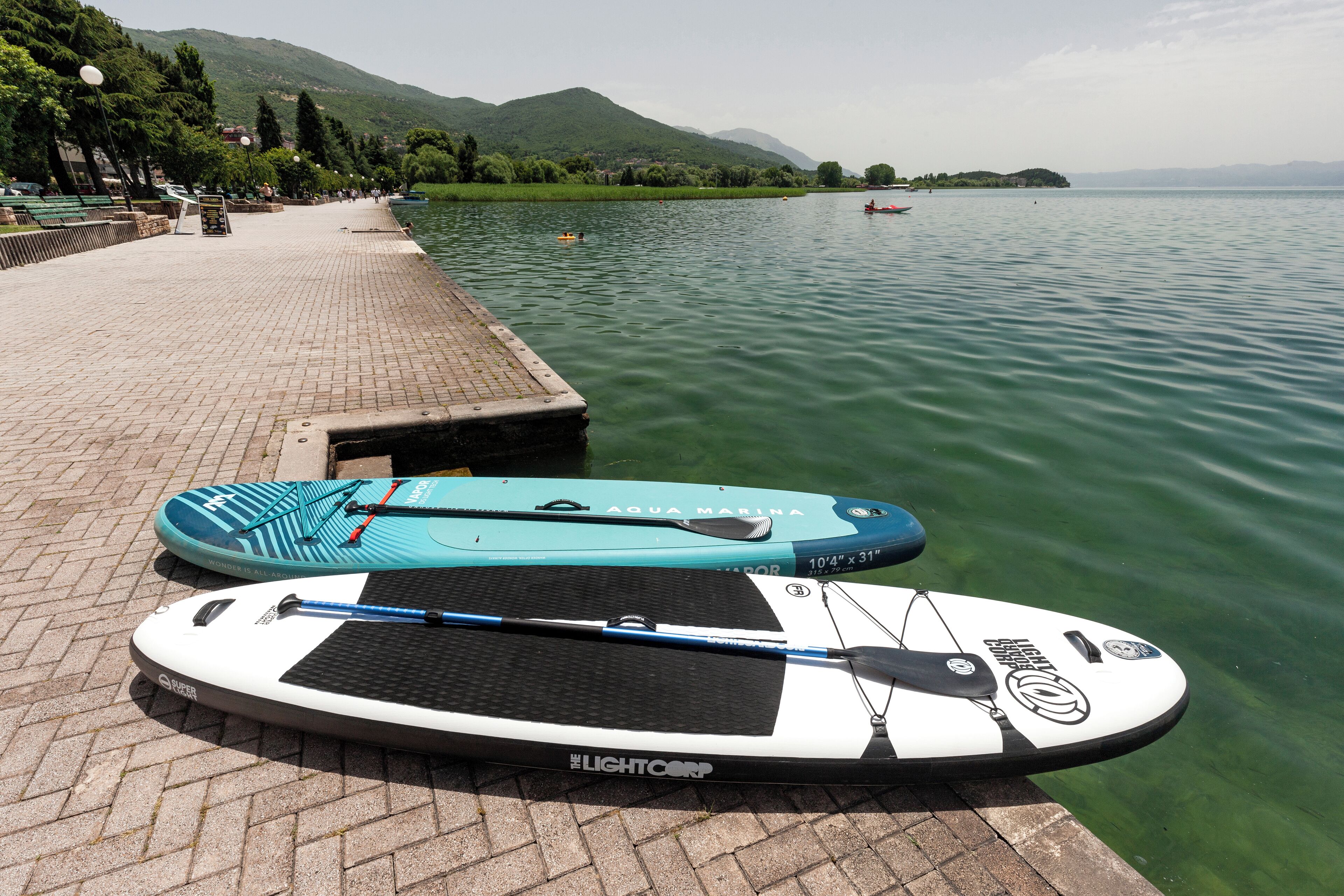 Dos tablas de paddle surf en un muelle junto a un lago tranquilo con montañas al fondo.