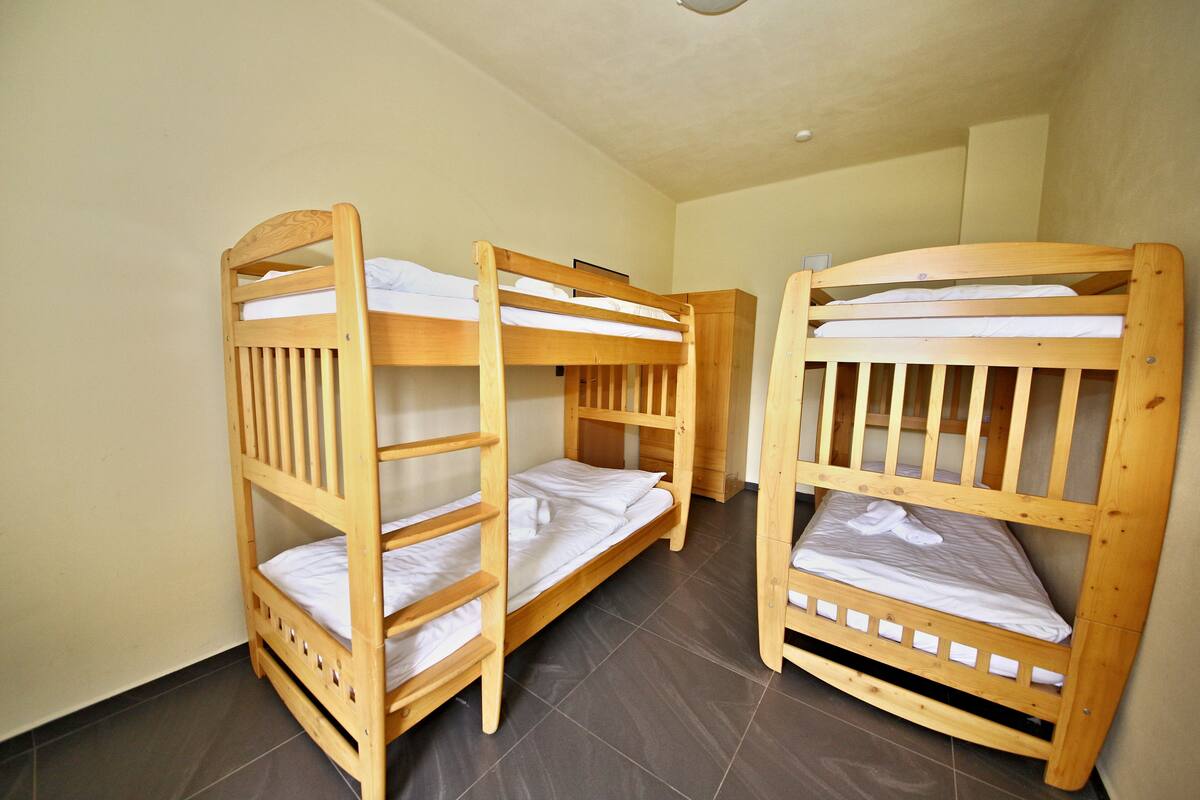 A room with three wooden bunk beds arranged in a row against a plain wall.