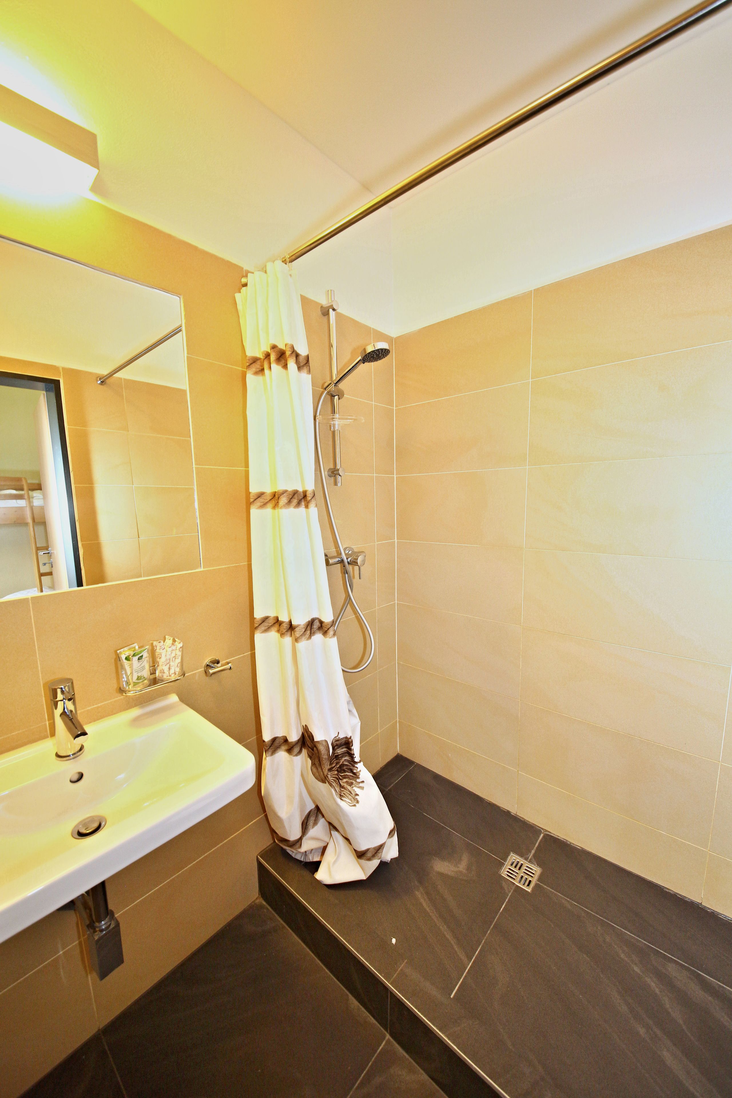 Ein Badezimmer mit Waschbecken, Spiegel, Dusche und gefliesten Wänden.