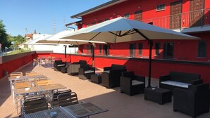 An outdoor patio with tables and chairs, umbrellas, and a red building in the background. - Residence Moscati (Avellino)