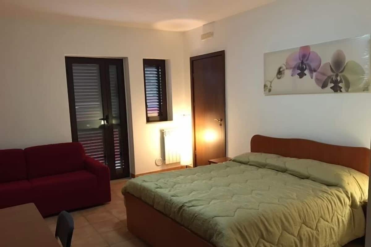 Um quarto com uma cama, um sofá vermelho, uma cadeira e um quadro de flores na parede.