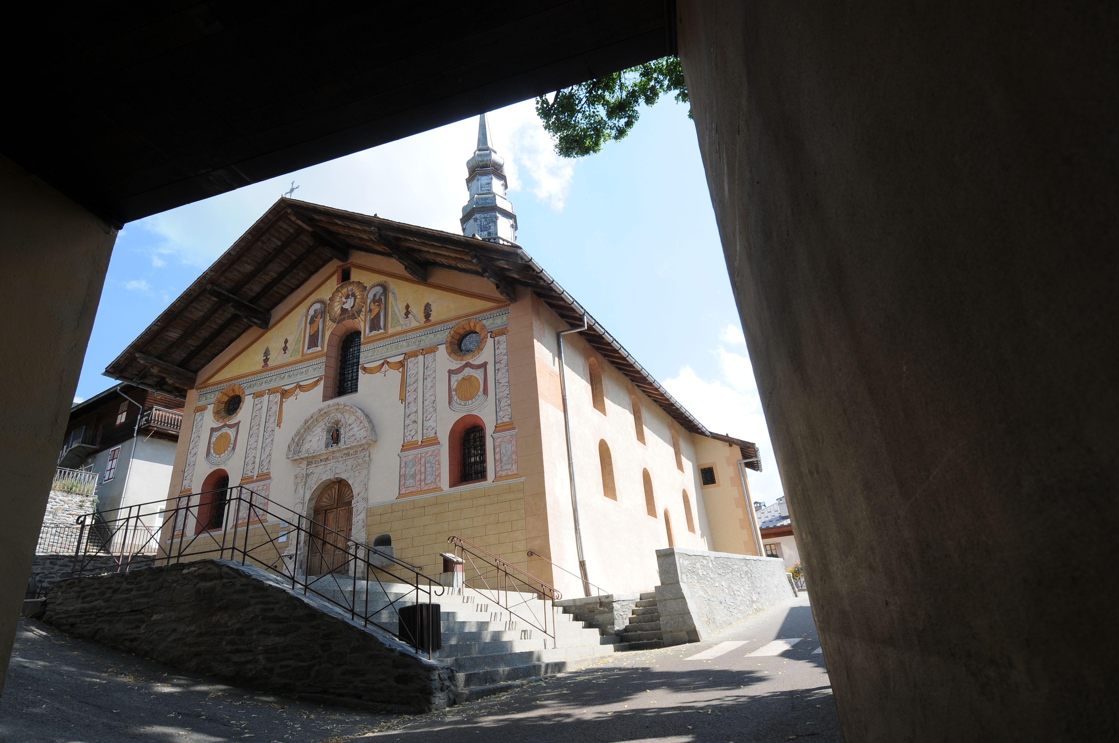A church with a bell tower, a staircase leading to the entrance, and a stone wall in the foreground.