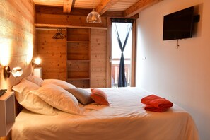A wooden cabin room with a bed, a TV mounted on the wall, and a window with curtains. - Chambres d'hôtes - La Pora (Hauteluce)