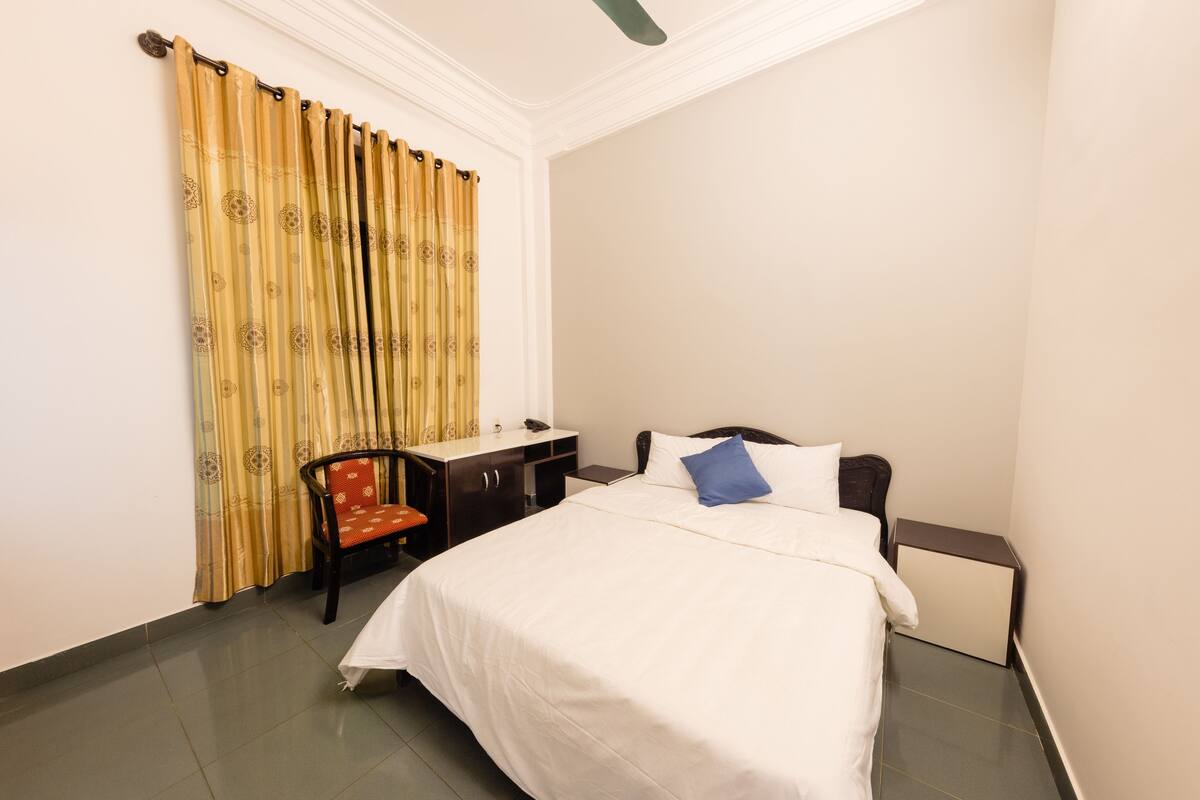 Una habitación de hotel con cama, escritorio, silla y ventana con cortinas.