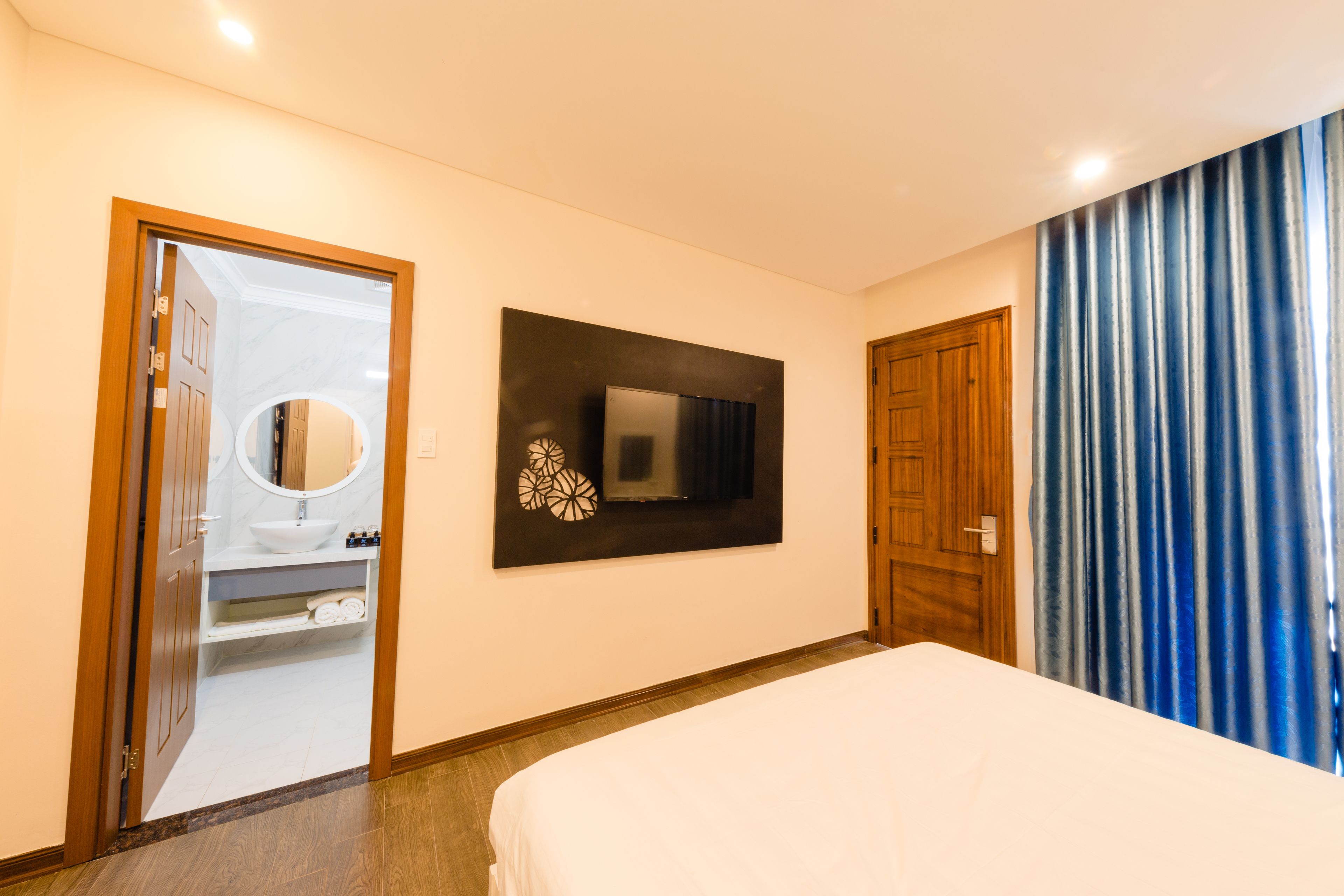 Habitación de hotel con cama, baño con lavamanos y espejo, televisor de pantalla plana montado en la pared y puerta de madera.