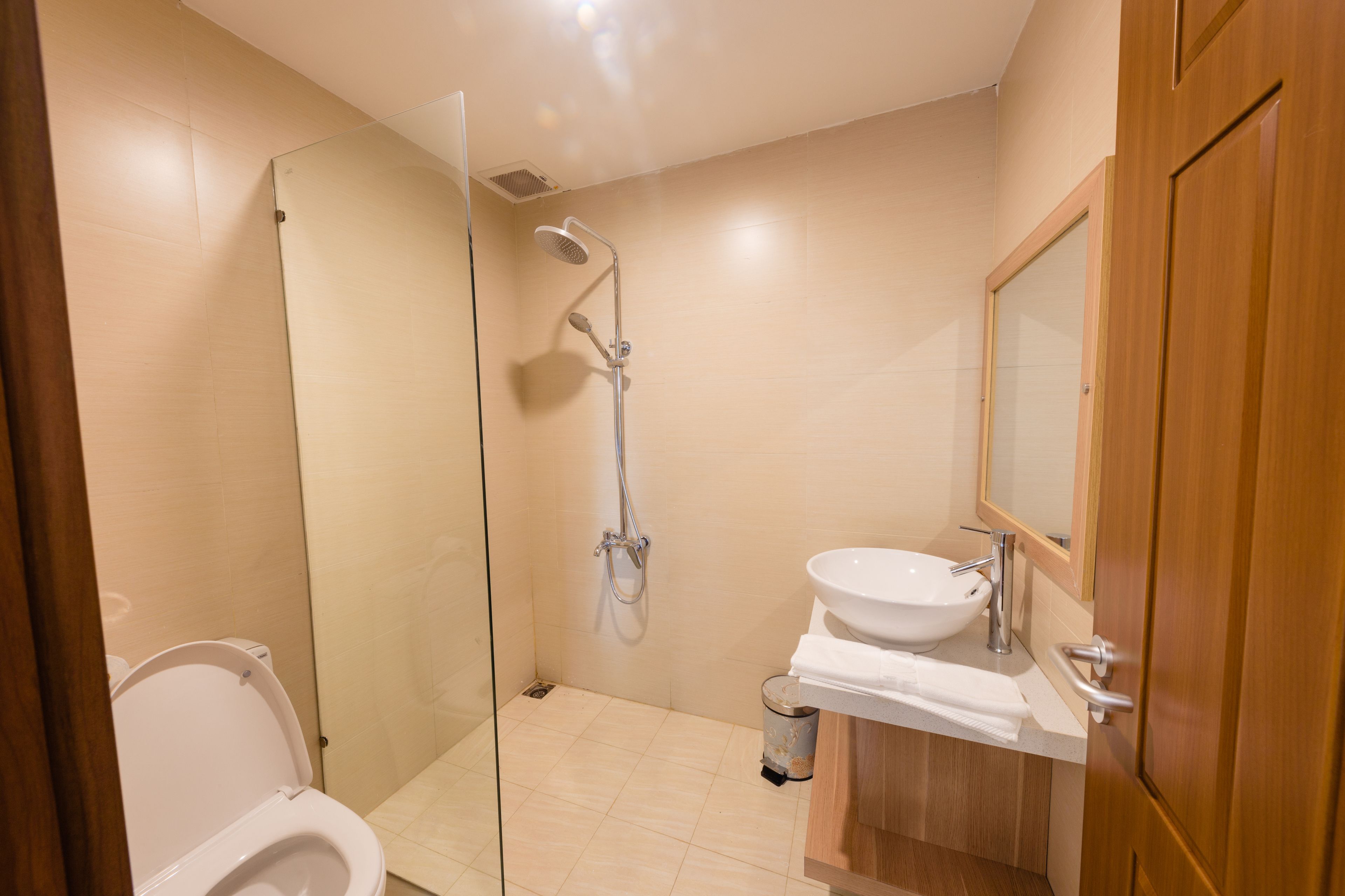 Un baño con ducha de vidrio, un lavamanos blanco y una puerta de madera.
