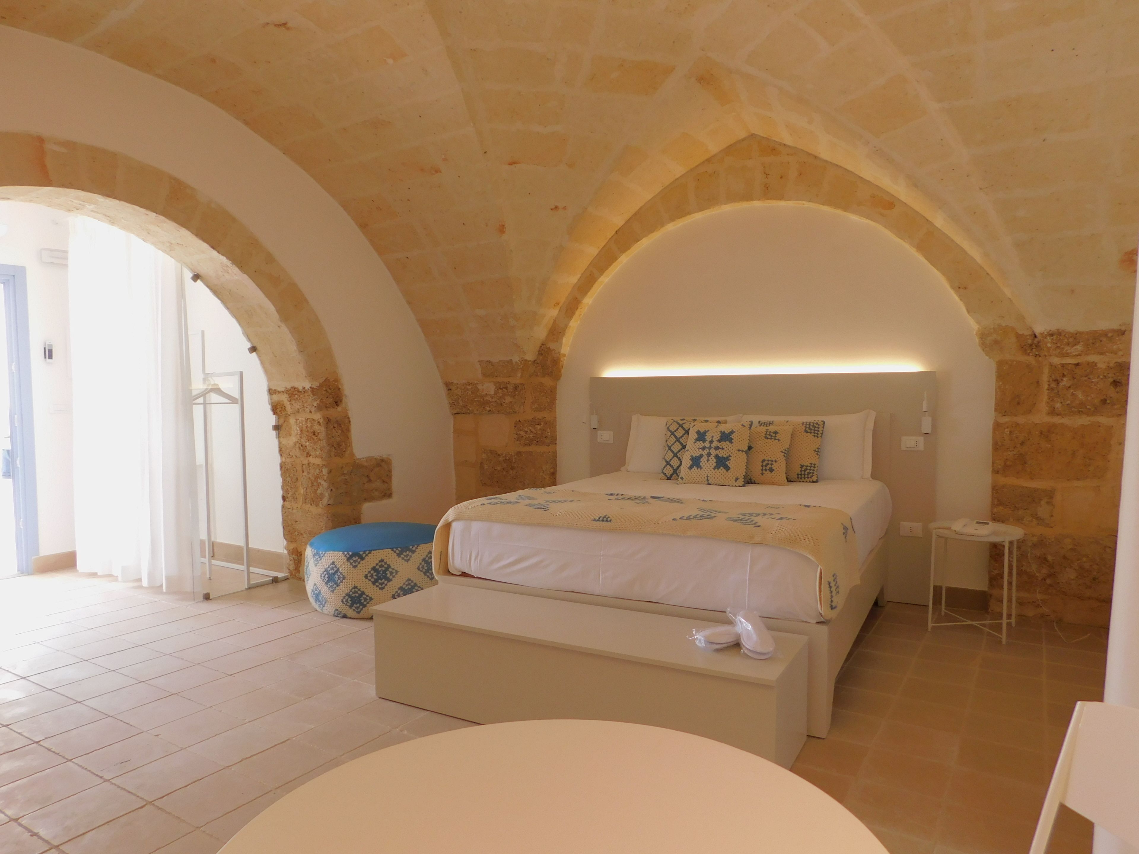 A bedroom with a stone arch ceiling, a bed with patterned pillows, a bedside table with a phone, and a bench.
