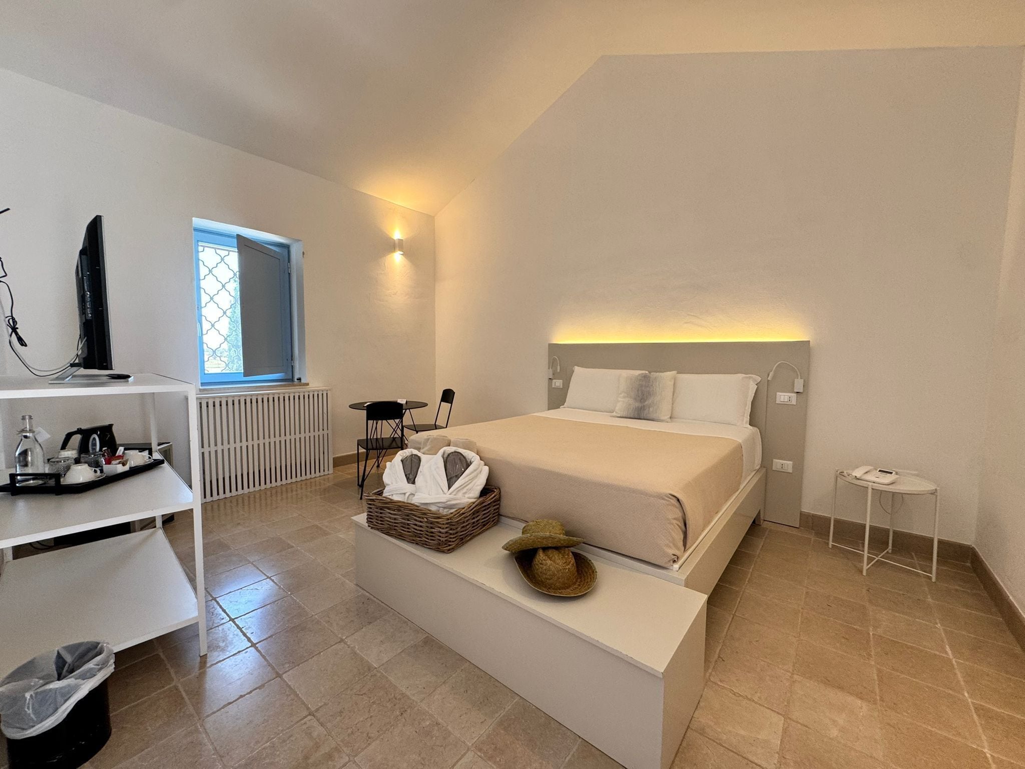 Une chambre d’hôtel avec un lit, une table de chevet, une petite table ronde, un radiateur, une télévision et une fenêtre donnant sur un paysage agréable.