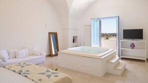 A modern bedroom with a large bathtub, a sofa, a television, and a view of the outdoors. - Masseria Malvindi (Mesagne)