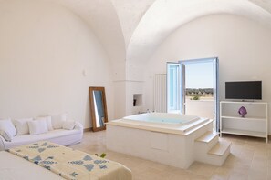 Un dormitorio moderno con una bañera grande, un sofá, un televisor y vistas al exterior.