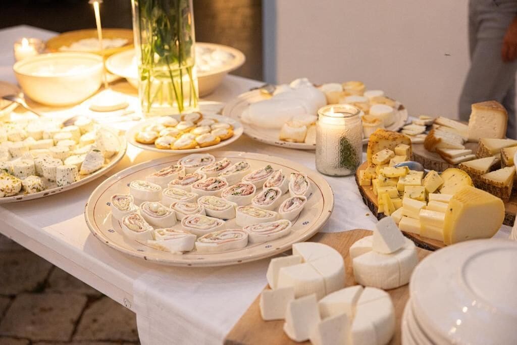 A table with various cheese and cheese-based appetizers, including cheese cubes, slices, and rolled items, arranged on a white tablecloth.