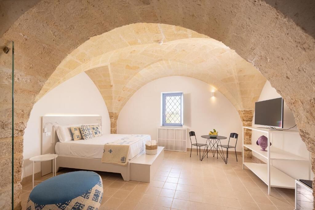 Un dormitorio acogedor con arco de piedra, cama, mesita, televisor y ventana.