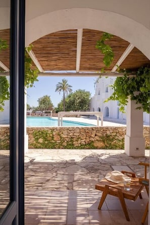 An outdoor patio with a pool, stone walls, and a view of a white building with arches. - Masseria Malvindi (Mesagne)