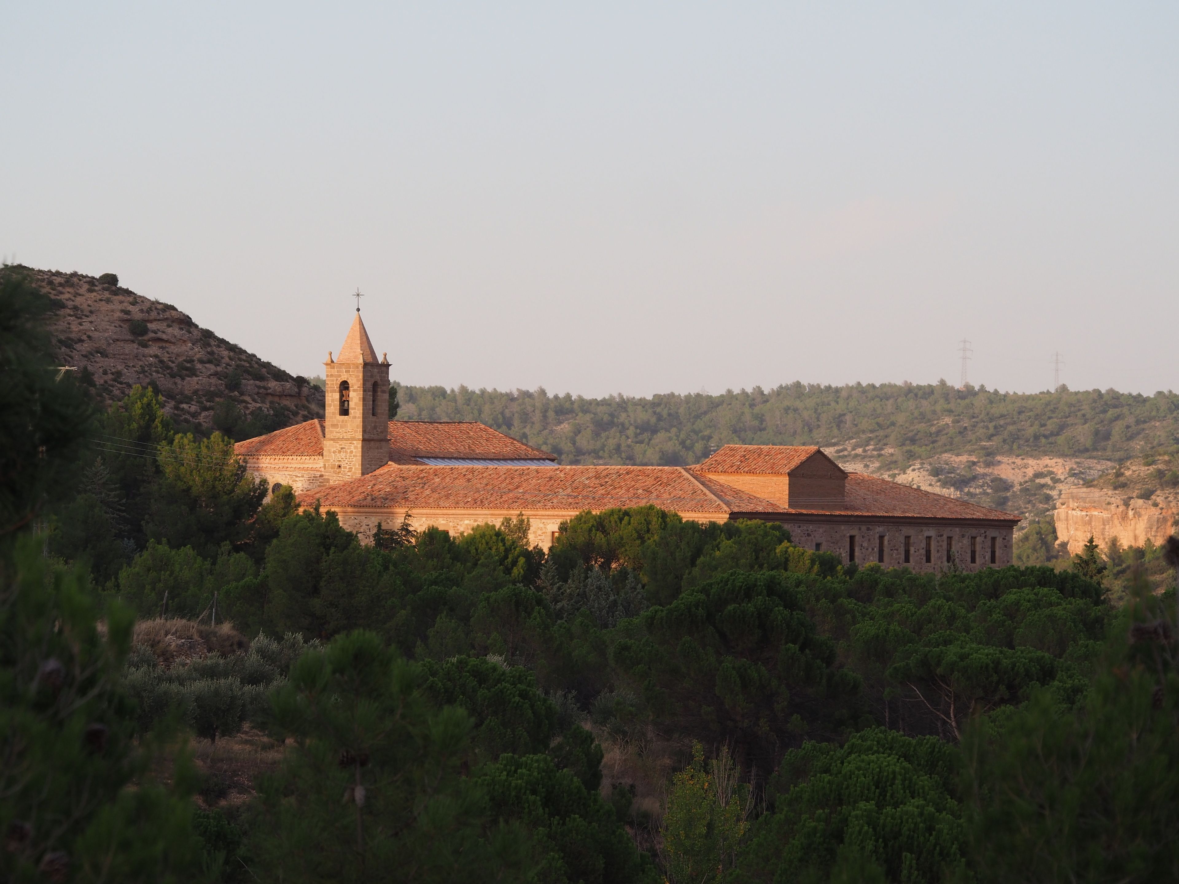 A historic building with a prominent bell tower, surrounded by dense forest and hills.